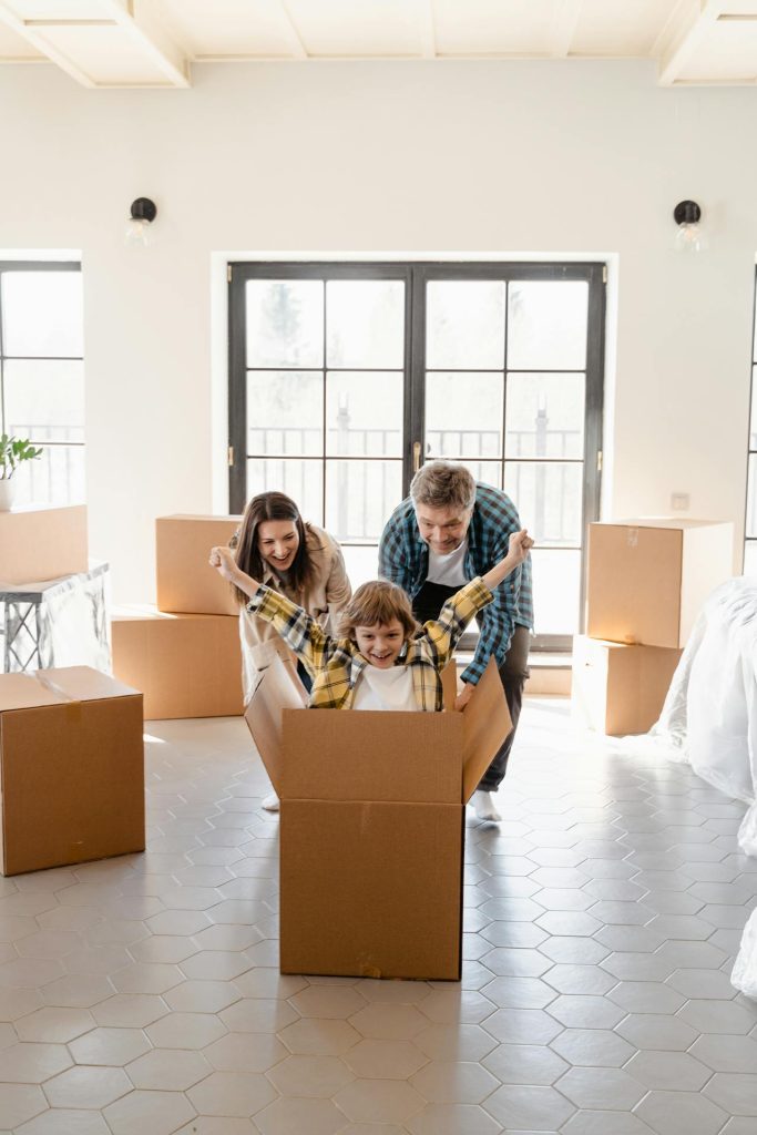 A child playing in a large cardboard box. His parents also play along.