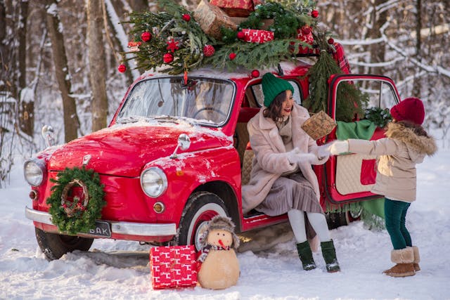 A mother and child talking by a small red car.